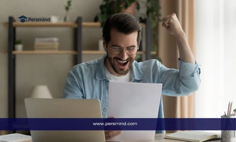 شاب يقرأ ورقة أمام الحاسوب ويُظهر فرحة النجاح – صورة معبرة عن أهمية كتابة رسالة حافز قوية للتقديم على المنح الدراسية أو القبول الجامعي.