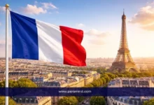 علم فرنسا يرفرف فوق مدينة باريس مع إطلالة واضحة على برج إيفل عند الغروب – صورة ممهدة لمقال مؤتمر التنمية العالمي في فرنسا.