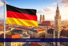 علم ألمانيا يرفرف فوق مدينة ميونخ مع إطلالة على ساحة ماريانبلاتز والمباني التاريخية – صورة مرافقة لمقال منحة NHR في ألمانيا للطلاب الدوليين.