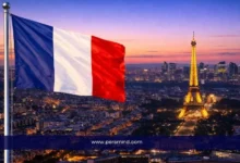 علم فرنسا يرفرف فوق مدينة باريس مع إطلالة على برج إيفل مضاء عند الغروب – صورة مرافقة لمقال المنتدى العالمي للديمقراطية في فرنسا.