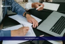 طلاب يكتبون ملاحظات بجانب لابتوب أثناء مناقشة، صورة تعبّر عن إعداد وكتابة خطة بحث أكاديمية.