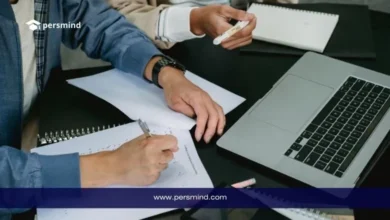 طلاب يكتبون ملاحظات بجانب لابتوب أثناء مناقشة، صورة تعبّر عن إعداد وكتابة خطة بحث أكاديمية.