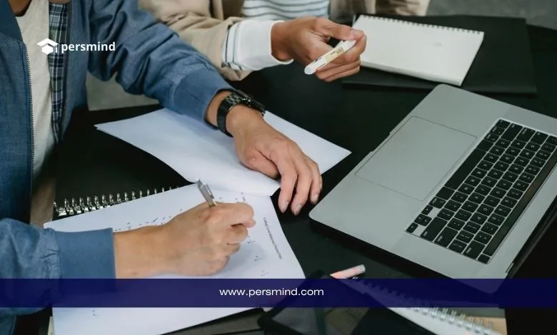 طلاب يكتبون ملاحظات بجانب لابتوب أثناء مناقشة، صورة تعبّر عن إعداد وكتابة خطة بحث أكاديمية.