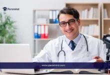 طبيب مبتسم يجلس أمام حاسوبه في مكتبه يمثل فرص منح لدراسة الطب بدون ايلتس لعام 2025