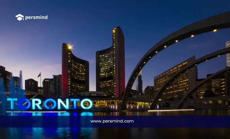 لافتة مضيئة تحمل كلمة TORONTO في ميدان ناثان فيليبس سكوير مع مبنى بلدية تورنتو في الخلفية أثناء الغروب.