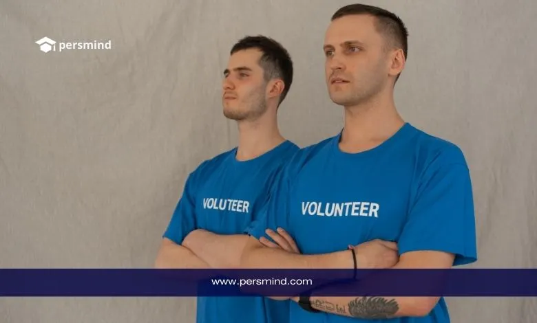 متطوعان يرتديان قمصانًا زرقاء مكتوبًا عليها VOLUNTEER يقفان بثبات وذراعاهما متشابكتان أمام خلفية محايدة – persmind.