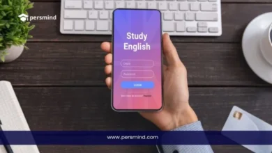 شخص يحمل هاتفًا ذكيًا تظهر عليه شاشة تطبيق بعنوان "Study English" كورس إنجليزي مجاني، فوق مكتب يحتوي على لوحة مفاتيح ودفتر وفنجان قهوة.