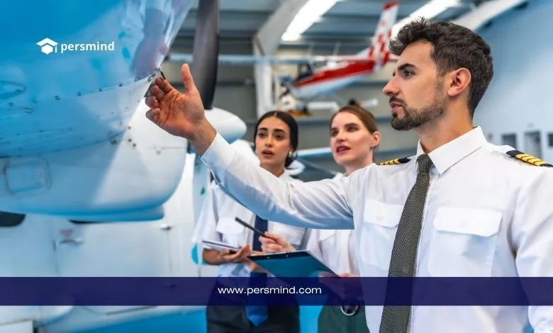 طلاب طيران يتدربون في أكاديمية طيران الإمارات داخل ورشة صيانة الطائرات، أحدهم يرتدي زي الطيار ويتفقد محرك الطائرة برفقة زملائه.