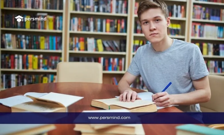 طالب دولي يدرس في مكتبة جامعية ويكتب ملاحظات على الكتب استعدادًا للتقديم في منحة الجامعة القاسمية