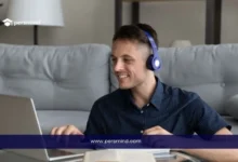 رجل يرتدي سماعات رأس ويتابع درسًا عبر الكمبيوتر المحمول أثناء تدوين الملاحظات، في صورة تعبيرية لدورة تعلم اللغة الإنجليزية للسفر.