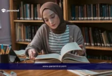 طالبة تدرس في مكتبة جامعية ضمن منحة جامعة هلسنكي وهي تقرأ كتابًا كبيرًا على طاولة خشبية.