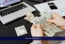 صورة طالب يقوم بعدّ الدولارات أمام جهاز لابتوب أثناء التحضير لفتح الحساب البنكي المغلق للدراسة في ألمانيا