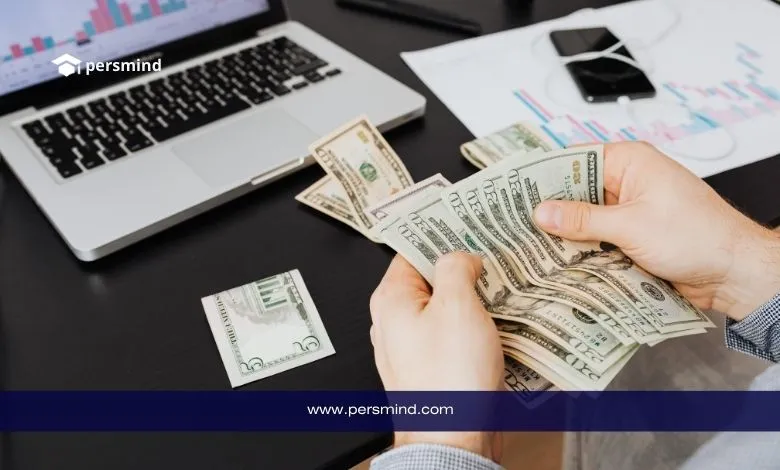 صورة طالب يقوم بعدّ الدولارات أمام جهاز لابتوب أثناء التحضير لفتح الحساب البنكي المغلق للدراسة في ألمانيا