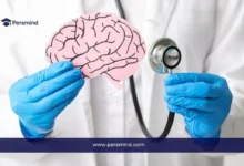 طبيب يرتدي قفازات طبية يحمل نموذجًا ورقيًا للدماغ ويستخدم سماعة طبية، في سياق توضيح دراسة الطب النفسي وتخصصات الصحة العقلية.