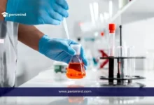 فني مختبر يرتدي قفازات طبية يقوم بمناولة دورق يحتوي على محلول برتقالي داخل مختبر، في سياق دراسة الطب النووي والتجارب المخبرية.