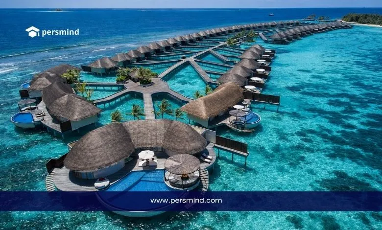 صورة جوية لمنتجع فاخر في جزر المالديف يضم فللًا فوق الماء وسط بحر تركوازي، مع ظهور شعار Persmind في الأعلى ورابط الموقع في الأسفل، تُستخدم في مقال عقد عمل في جزر المالديف.