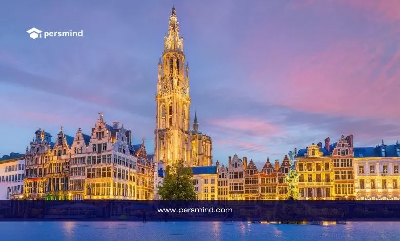 مشهد مسائي لمدينة أنتويرب في بلجيكا يظهر فيه برج الكاتدرائية والمباني التاريخية المضاءة على ضفاف النهر، مع شعار Persmind في الأعلى.