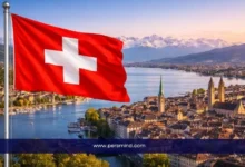 علم سويسرا يرفرف فوق مدينة سويسرية بإطلالة على البحيرة والجبال – صورة لمقال زمالة الصندوق الإنساني التابعة للمفوضية السامية لحقوق الإنسان.