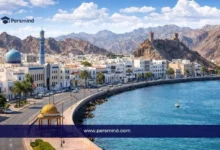 منظر نهاري لواجهة بحرية في مدينة مسقط بسلطنة عُمان مع مبانٍ بيضاء وجبال في الخلفية، ويُستخدم كصورة لمقال عن زمالة ICANN87 في سلطنة عُمان
